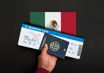 Hand holds passport and boarding pass with flag of Mexico