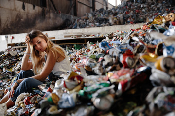 Young blonde nature pollution activist sits at huge trash dump. Looks at all human waste and...