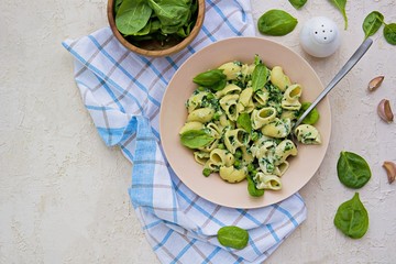 Obraz premium Spring green pasta with spinach and green peas in a creamy sauce in a beige clay plate on a light concrete background. Pasta Recipes. Italian food. Copyspace.