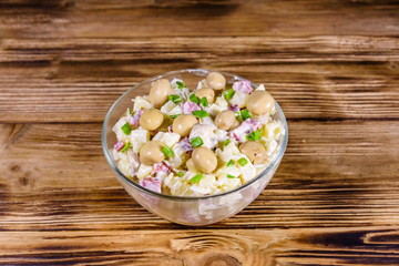 Salad with marinated mushrooms, sausage, onion, boiled potato and mayonnaise on a wooden table