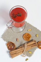 Red drink in a glass goblet. Anise stars float in it. Nearby on linen are pistachios, dried mandarin rings and cinnamon sticks.