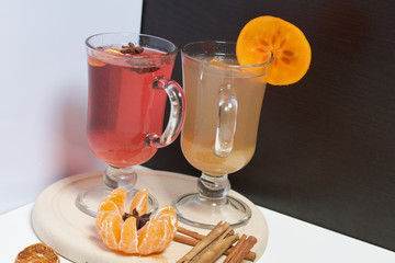 Drink red and yellow in glass goblets. Anise stars, a slice of persimmon float in it. Next to the linen fabric is peeled mandarin, dried mandarin rings, cinnamon sticks and anise stars.