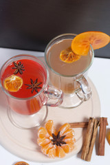 Drink red and yellow in glass goblets. Anise stars, a slice of persimmon float in it. Next to the linen fabric is peeled mandarin, dried mandarin rings, cinnamon sticks and anise stars.