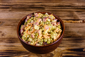 Salad with sausage, green pea, onion and carrot in glass bowl on wooden table
