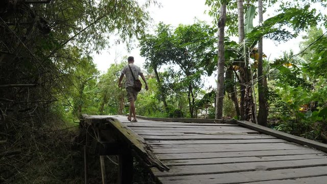 European tourist walks over wooden bridge in country side of Philipinnes