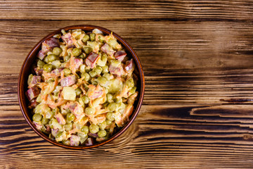 Salad with sausage, green pea, onion and carrot in glass bowl on wooden table. Top view