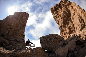 Man standing on the balance board on the one leg among the rocks in the mountains