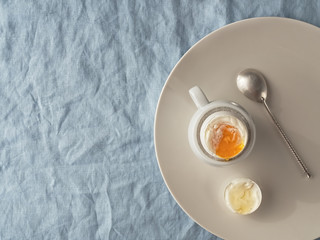 Light breakfast: soft-boiled egg on a ceramic plate, on a blue tablecloth. Flat lay. Copy space