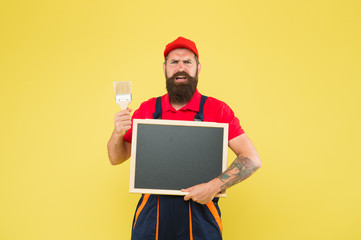 Man worker with paint brush. Builder regular worker. Repair and renovation. Quick repair. Creative decorator. Painting works. Bearded decorator laborer hold blackboard copy space. Repair tips