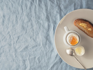 Obraz na płótnie Canvas Light breakfast: soft-boiled egg, toast with butter on a ceramic plate, on a blue tablecloth. Flat lay. Copy space