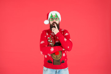 surprised male in xmas party glasses. happy new year. funny hipster knitted sweater. warm clothes for cold weather. winter holiday season. bearded man santa hat red background. merry christmas