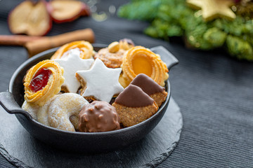 Various Christmas Cookies in a black bowl, on a black table with some Christmas decoration in the...