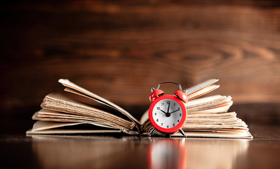 Old book and little alarm clock on wooden table