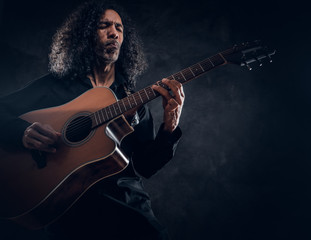Obraz premium Curly man with guitar is presenting his new acoustic masterpiece at studio.