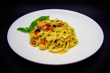 Pasta with salmon and olives on black background