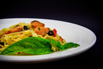 Pasta with salmon and olives on black background
