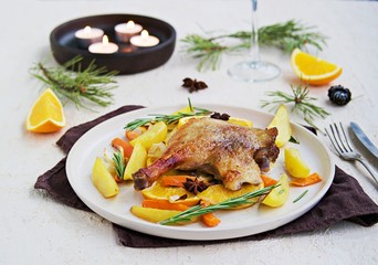 Roasted duck leg with potatoes, carrots and slices of orange on a ceramic plate on a light concrete background. Christmas and New Year dishes recipes. Duck recipes. French cuisine