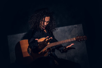 Obraz premium Charismatic rock singer is posing with his guitar while singing at dark studio.