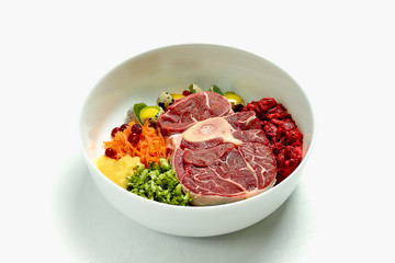 Natural dog food in big white bowl over white background. Beef meat, eggs and vegetables. Close up.