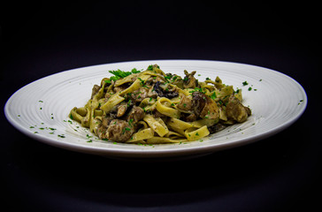 Pasta with mushrooms and pork on a black background