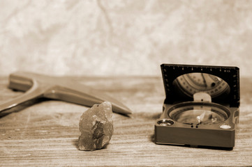A geologist's hammer, a compass, and a mineral interspersed with iron ore are laid out on a wooden table.