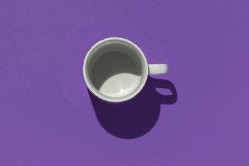 Empty tea cup on violet paper background. Coffee mug from above. Minimal concept. Dark shadow. Flat lay, top view.