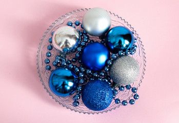 Christmas toys round shape next to the beads, trend color 2020 classic blue, in a plate, on a pale pink color
