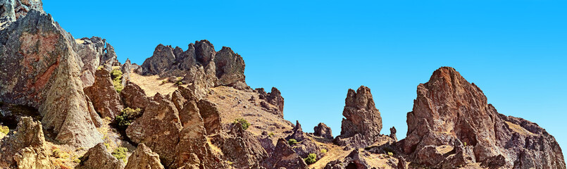 Fototapeta premium scenic rock formation of volcano mountain landscape against blue sky background. Panorama wide view of karadag mountain range in crimea. Outdoor wild nature panoramic wallpaper