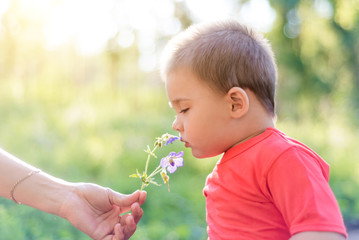 a little child in the Park sniffing a flower, a child enjoying nature on a Sunny summer day. the concept of happy childhood and kindness. cute kind child on the street with a flower