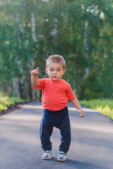 the little kid shows one finger with his hand. cute cheerful kid in a red t-shirt walking in the Park. one-year-old child portrait.