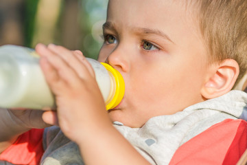 adorable baby drinking milk from the bottle on the street in the Park sitting in a wheelchair