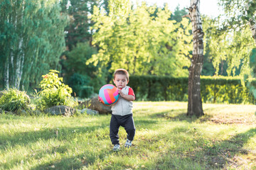 Naklejka premium a little boy playing in the street with a ball. cute cheerful baby walking in the Park. happy child