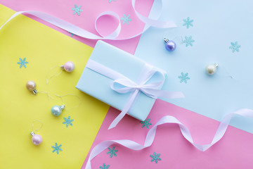 a gift in a blue box tied with a white ribbon on a pink paper background sits next to small shiny Christmas balls of loop shades