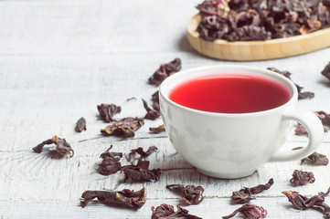 White cup of healthy hibiscus tea with dried hibiscus flowers on white wooden background, winter hot drink concept for cold and flu 