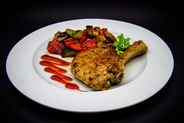Pork loin with baked vegetables on black background