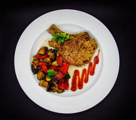 Pork loin with baked vegetables on black background