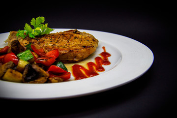 Pork loin with baked vegetables on black background