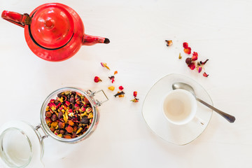 Top view of cup of tea, red teapot, herbal and infusion elements against white background. Flat lay, breakfast, food, and wellness concept. 