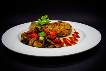 Pork loin with baked vegetables on black background