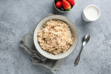 Healthy breakfast porridge oats or oatmeal in bowl on concrete background, table top view shot. Clean eating concept