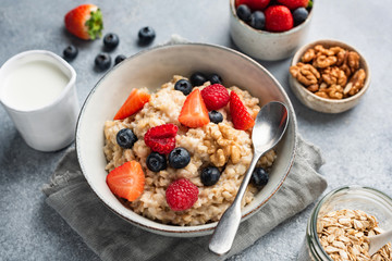 Oatmeal with blueberries, raspberries, strawberries and walnuts in a bowl. Healthy breakfast food, vegan diet concept. Closeup view