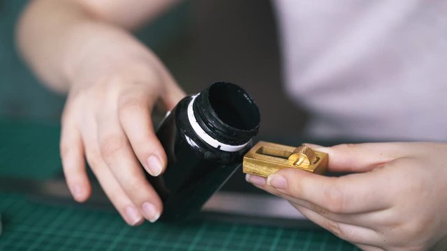 CU: Skilled designer pours black leather paint into pure copper holding small bottle in hand extreme close view