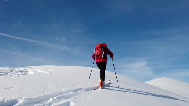 Ski mountaineer climbs a snowy mountain over blue clear sky. Winter season, sunny day. Concepts: achieve a personal goal, exploration, new horizons.