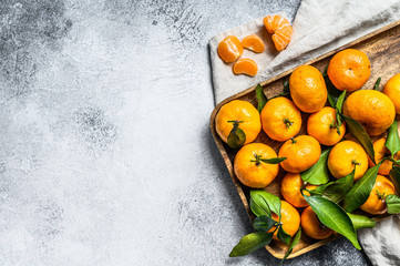Tangerines (oranges, mandarins, clementines, citrus fruits) with leaves in wooden bowl. Gray...