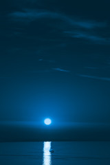 Dark blue sky with rare clouds and a bright full moon over the seascape