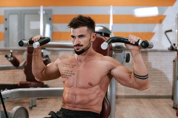 Fototapeta na wymiar Shirtless muscular young man doing barbell bench press exercise at the gym