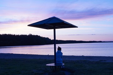 Young woman sits on a night deserted beach under a beach umbrella