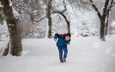 Fototapeta na wymiar Cute boy walking through the park, snow falling on him, slightly bending