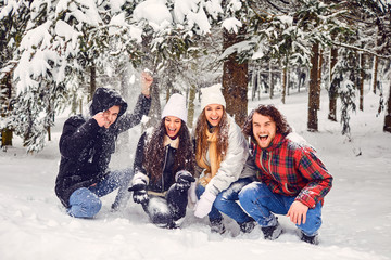 Friends under a tree with falling snow in a park in winter.