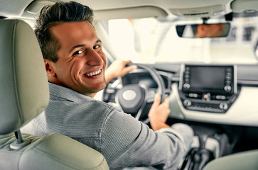 The young man behind the wheel. Rear view, young man driving his car, looking at camera.